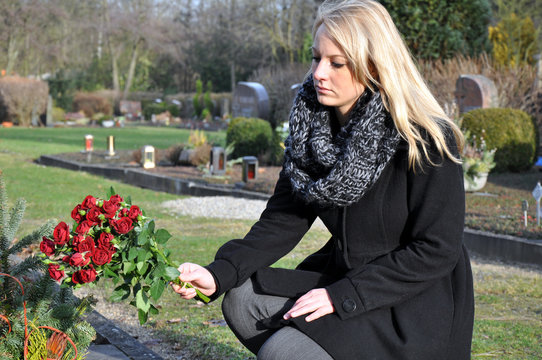 Frau legt Blumen auf Grab