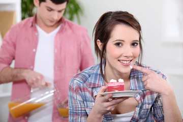 girl eating strawberry gateau with boyfriend in background
