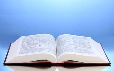 Obraz premium Open book on reflective surface of table on blue background