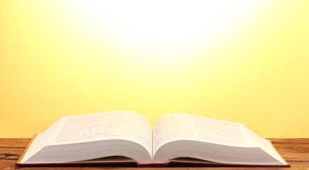 Open book on wooden table on yellow background