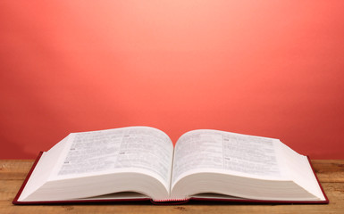 Open book on wooden table on red background