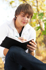 Fototapeta premium Man writing on His Organizer on a Bench Outdoors