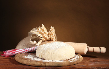 Dough and bags with flour on wooden table on brown background