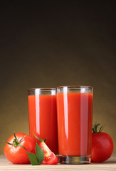 Tomato juice in glass and tomato on wooden table on brown backgr