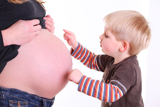 kleiner sohn spielt mit dem babybauch der mutter
