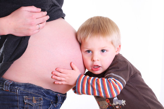 kleiner bruder horcht am babybauch der mutter