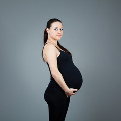 Portrait of pregnant brunette woman on grey background.