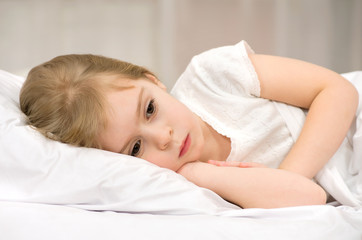 The sad little girl lying in bed