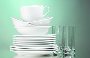 Clean plates, cup and glasses on green background