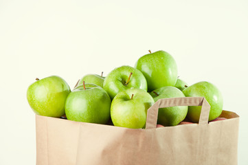 Grocery bag full of green fresh apples, over white background