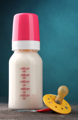 bottle of milk and soother on wooden table on blue background