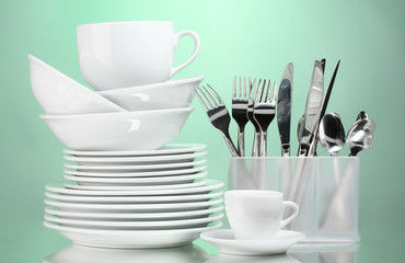 Fototapeta na wymiar Clean plates, cups and cutlery on green background