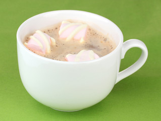 Cup of cappucino with marshmallows on green background