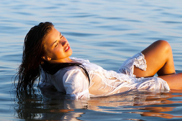 The attractive girl in a white wet transparent dress laying  in