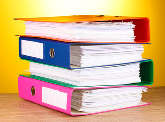 bright office folders on wooden table on yellow background.