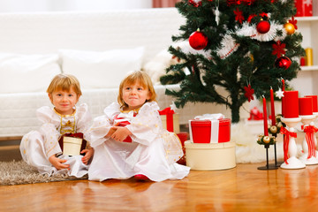 Obraz na płótnie Canvas Dwie dziewczyny bli¼nięta siedzi z prezentami w pobliżu choinki