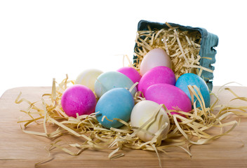 Small basket with colorful eggs spilling into straw