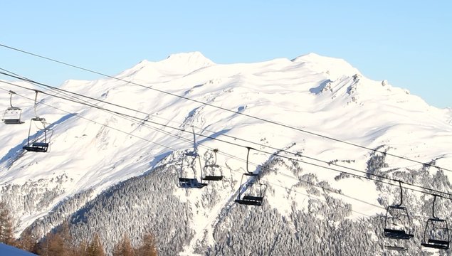 Empty ski lift chairs moving against snowy mountain in Alps, early morning before opening time, skiing concept