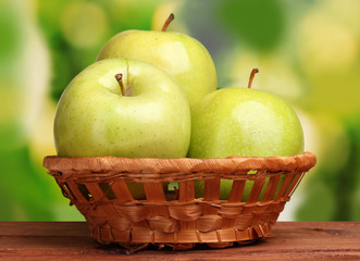 juicy green apples in basket on wooden table on green background