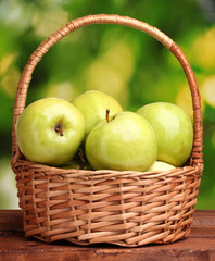 juicy green apples in basket on wooden table on green background