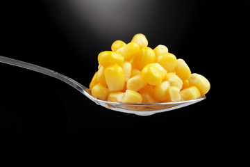 spoon with sweet corn over black