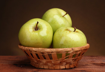 juicy green apples in basket on wooden table on brown background