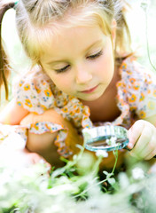 Little girl with magnifying glass looks at flower