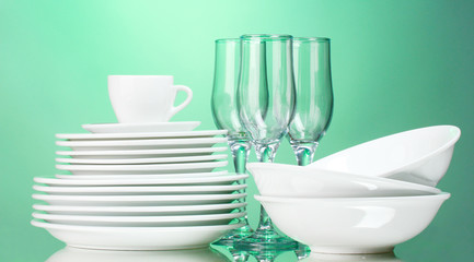 Clean plates, cup and glasses on green background