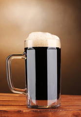 dark beer in a mug on wooden table on brown background