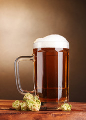 beer mug and green hop on wooden table on brown background