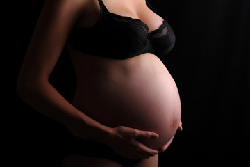 Pregnant woman touching her belly with hands, dark barkground