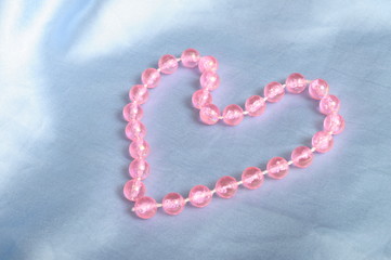 Obraz premium Heart shaped pink pearls child's necklace on blue tissue