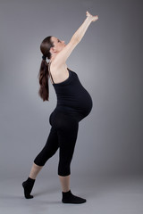 Obraz premium Pregnant woman doing gymnastic exercises on grey background.