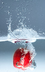 Red apple splashing into water on blue background