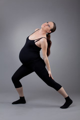 Fototapeta na wymiar Pregnant woman doing gymnastic exercises on grey background.