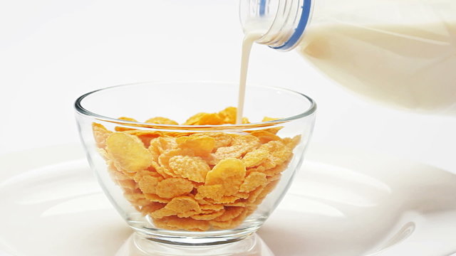 Corn flakes in a glass bowl pouring with milk over white
