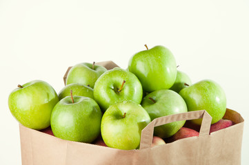 Shopping paper bag full of green apples isolated over white