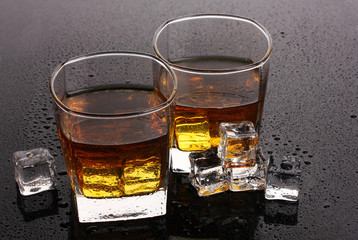 two glasses of scotch whiskey and ice on grey table