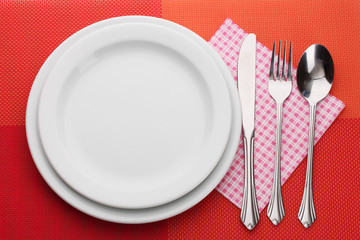 White empty plate with fork, spoon and knife on a red tablecloth