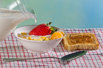 Milk puring down into fresh fruit and corn flakes