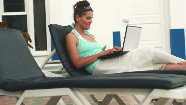 Woman with laptop sitting on sunbed, dolly shot