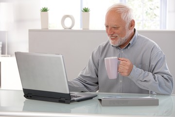Elderly man working on laptop smiling