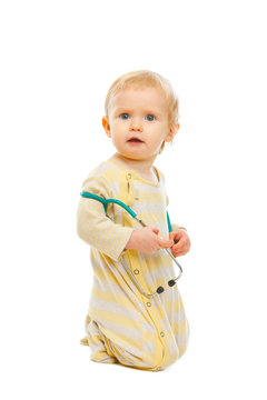 Confused baby with stethoscope sitting on floor