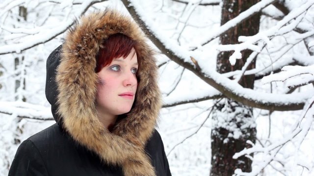 Girl in fur hood looks at falling snow