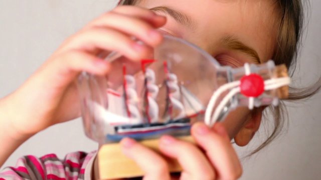 Girl hold and looks at model of tallship in glass bottle