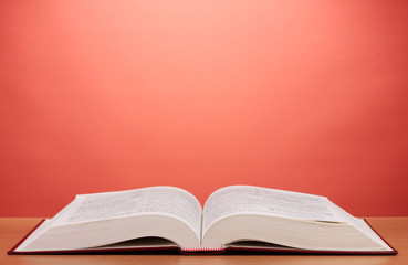 Open book on wooden table on red background