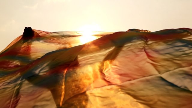 woman against sky and sun has hold thin shawl which waves