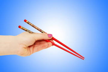 Hand holding choipsticks on gradient