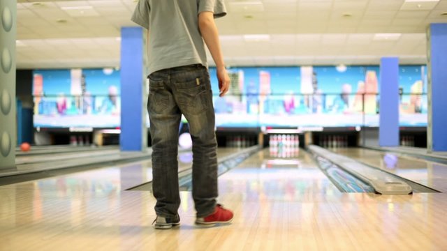 boy throws bowling ball to beat skittles, view from behind