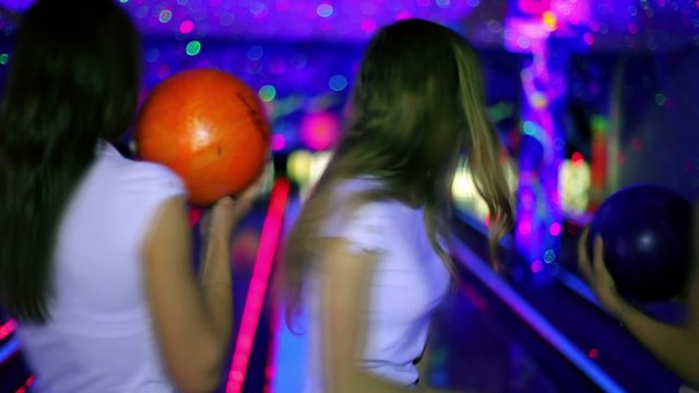 Three girls stand with bowling balls and then throw it